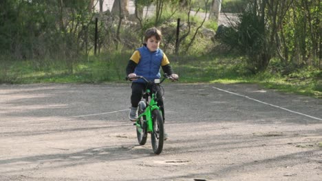 slow motion of greek caucasian boy, riding his bicycle on cement ground, passing out of the screen