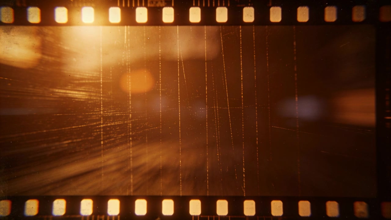 Projector projecteert een van achteren verlichte 35mm filmstrip, waarop tandwielgaten, krassen, stof en amberkleurige bokeh te zien zijn.