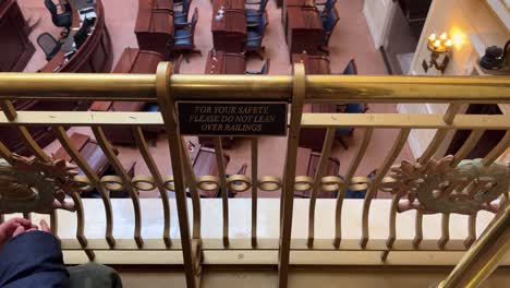 looking at a sign that says, for your safety please do not lean on railing with person or kid sitting in front of a brass railing that over looks senate chamber in utah state capital