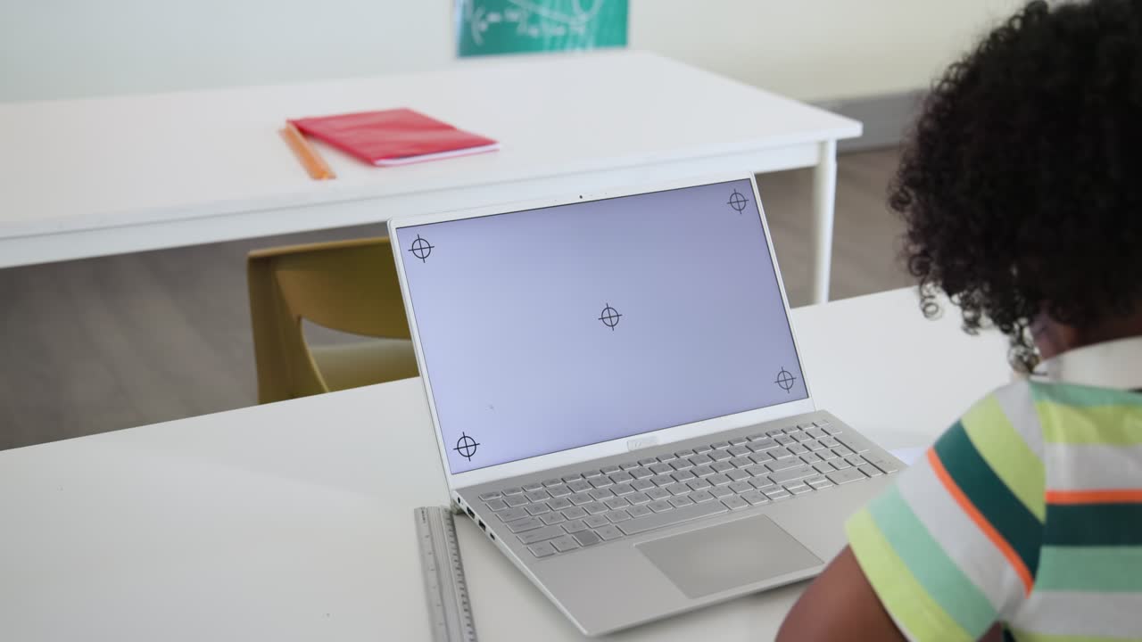 Studente scrive su un foglio con una matita alla scrivania, camera che fa una panoramica a sinistra, rivelando un laptop che esegue un'attività