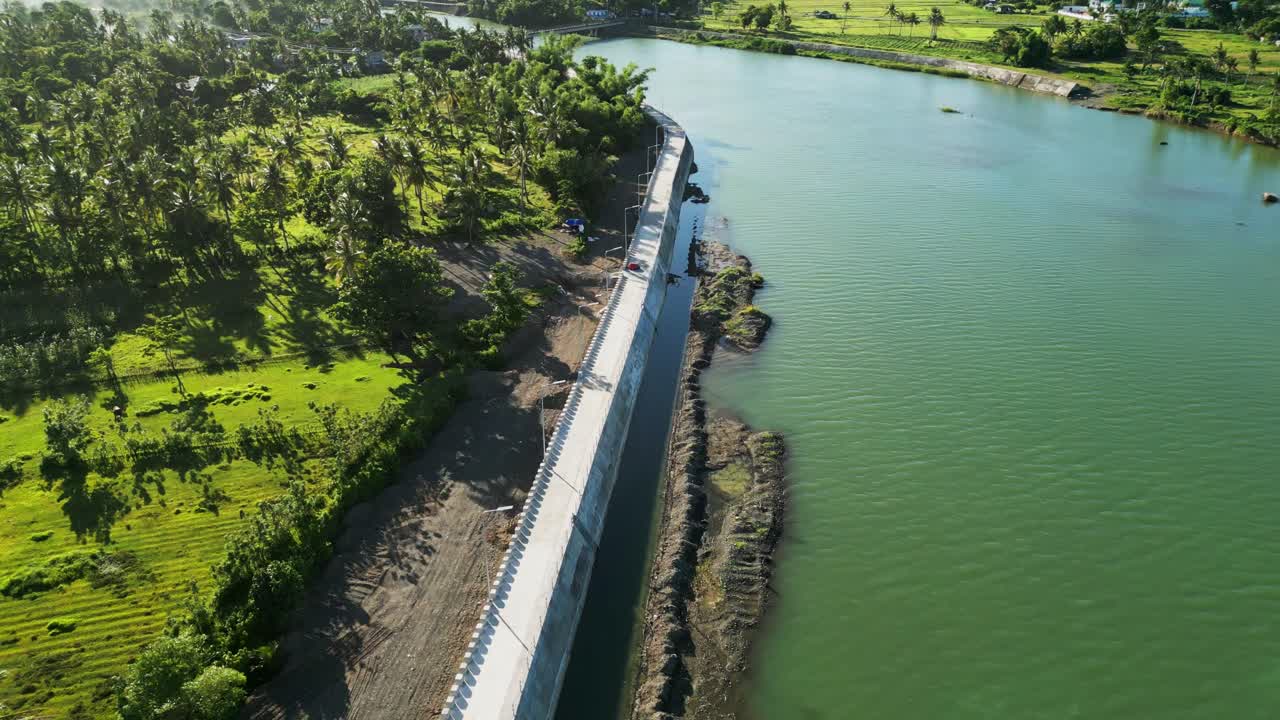 Stunning aerial flyover shot of a riverbank dike along wide river and lush island greenery at Pajo Baguio, Virac, Catanduanes, Philippines