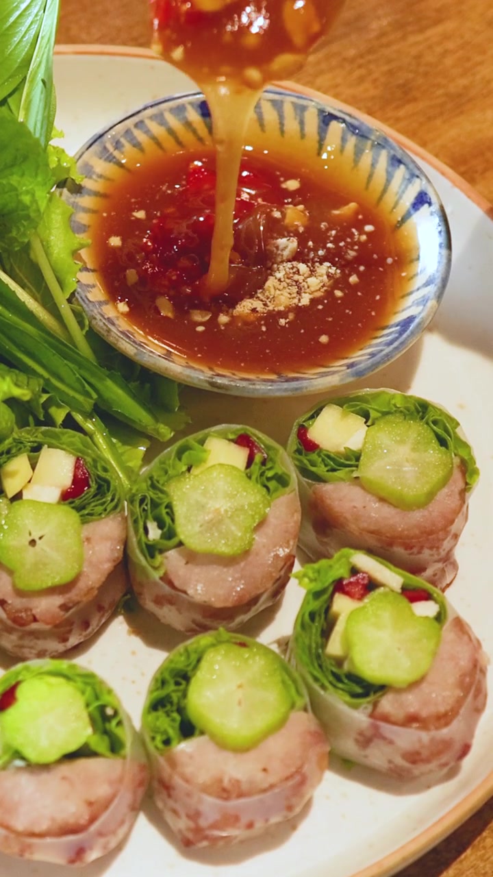 Cận cảnh gỏi cuốn Việt Nam với nước chấm đang được chuẩn bị. Màu sắc rực rỡ, nguyên liệu tươi ngon và hành động rót nước chấm sống động