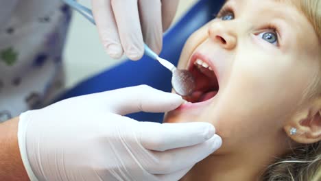 a dentist in medical gloves using a mirror examines the teeth of a little girl patient. children's dental clinic