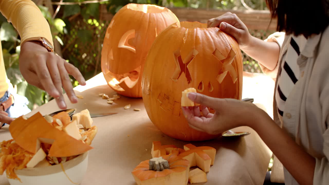 Carving pumpkins on a porch, two multiracial female friends creating festive halloween decorations
