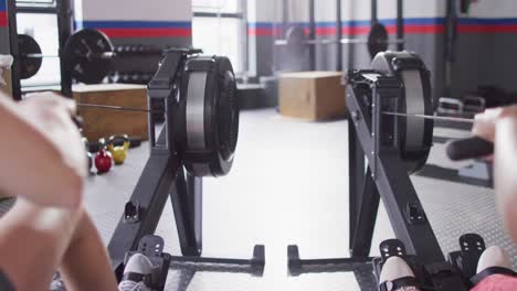 Video-of-rear-view-of-two-diverse-women-on-rowing-machines-working-out-at-a-gym