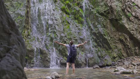 man with backpack spreading hands in front of waterfall.