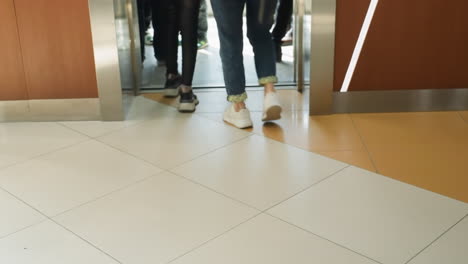 a dynamic first-person view captured with a handheld camera, showing the lower half of various people walking into an elevator. the scene focuses on the movement and diversity of footwear