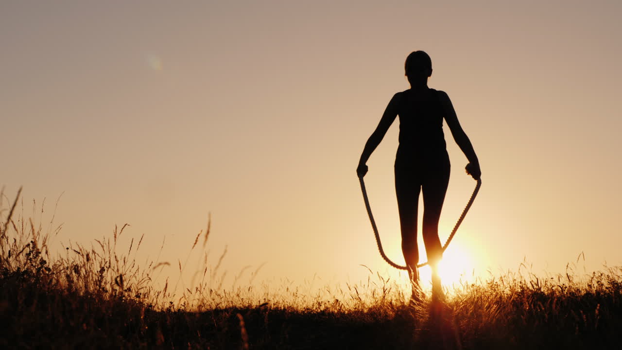 entrenando al aire libre - una silueta de una mujer saltando sobre una cuerda al atardecer