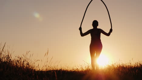 training in the fresh air - a silhouette of a woman jumping over a rope at sunset