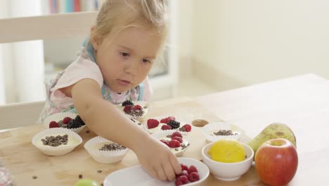 Girl-putting-berries-on-muffins-on-table