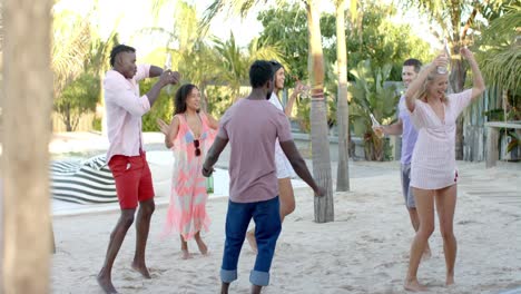 feliz grupo diverso de amigos bailando sosteniendo cócteles en la playa