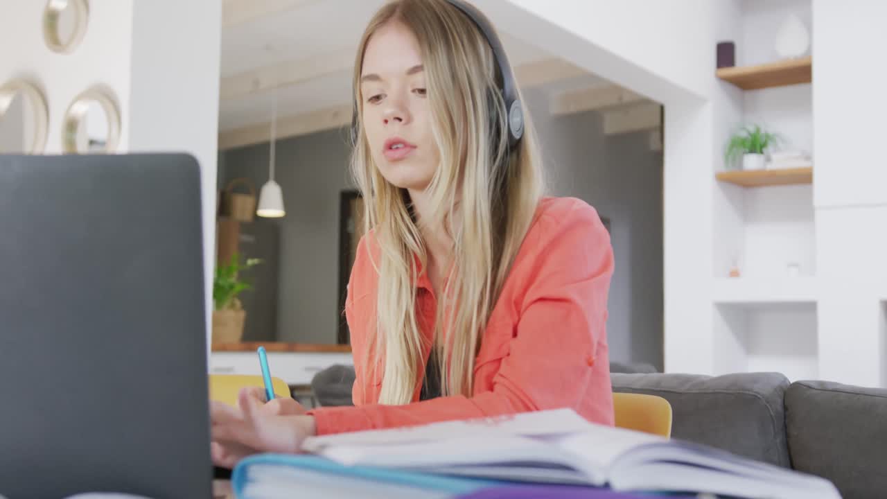 una adolescente caucásica con auriculares y usando una computadora portátil en casa, en cámara lenta