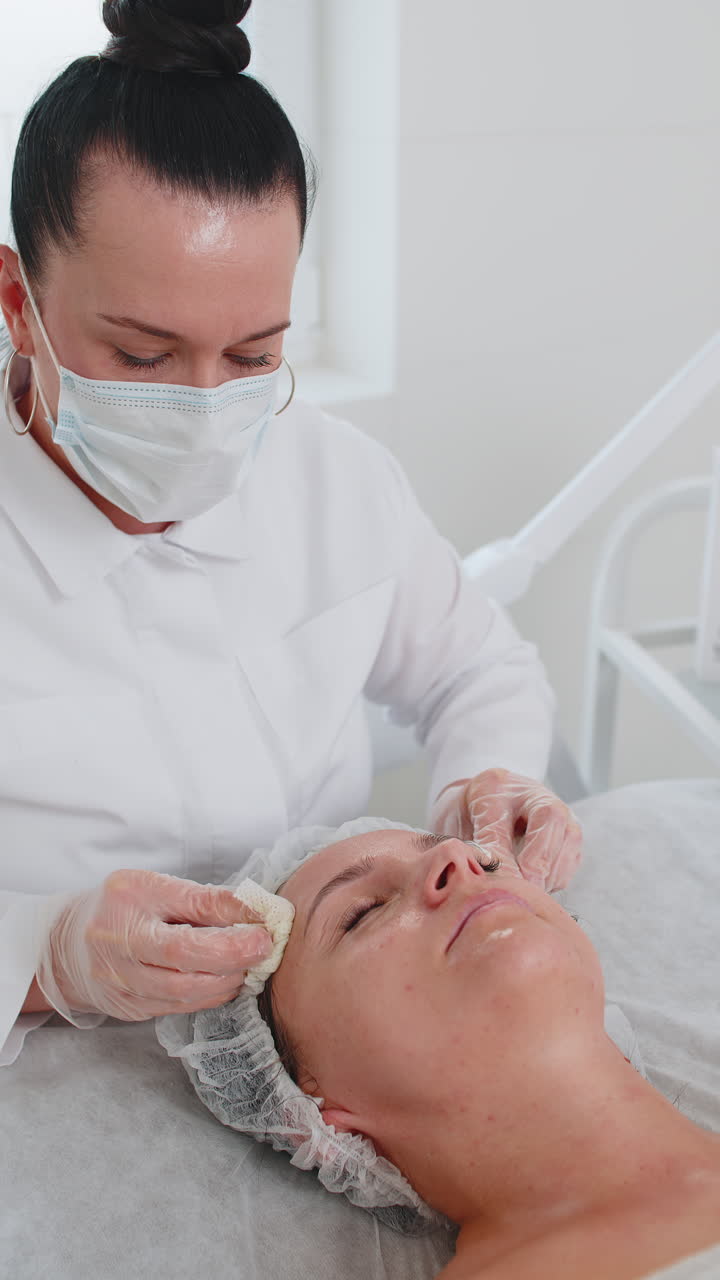 Una dottoressa cosmetologa pulisce viso e collo di una donna durante una procedura di pulizia con dischetti di cotone in una clinica estetica