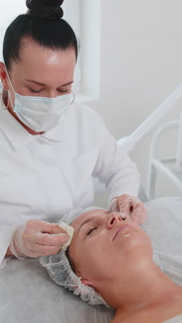 cosmetologist doctor wipes woman face and neck cleaning procedure with cotton wipes in beauty clinic