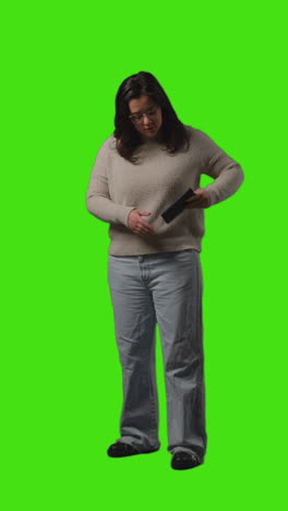 Vertical-Video-Full-Length-Shot-Of-Young-Woman-Answering-Call-On-Mobile-Phone-Standing-Against-Green-Screen