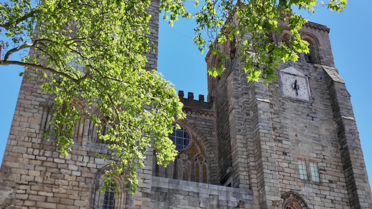 Green spring leaves frame the imposing Cathedral of Evora, a historic landmark in Évora, Portugal, on a bright sunny day