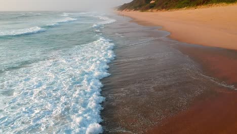 Playa-Prístina-Con-Olas-Azules-Rompiendo,-Tiro-Aéreo-De-Empuje-Hacia-Adelante-Bajo