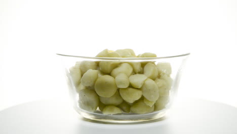 a glass bowl of macadamia nuts rotating clockwise on a white background