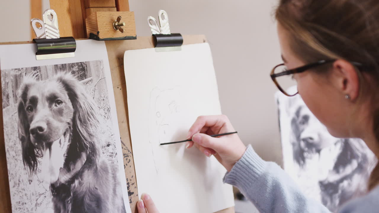 십대 여성 예술가 가 석탄 에 있는 사진 에서 개 의 그림 을 그리는 좌석 에 앉아 있다