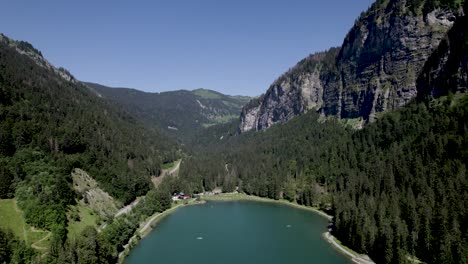 High-altitude-Montriond-lake-seen-from-above-with-rising-rock-peaks-above-pine-tree-forest