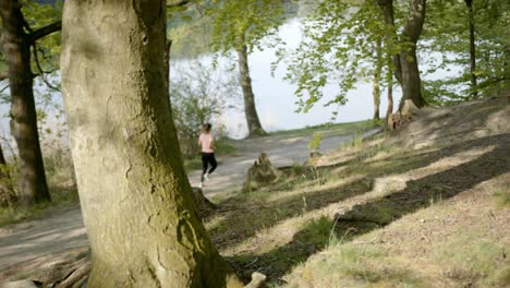 woman running through woods near river viewed from behind tree