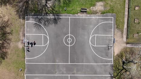 Una-Vista-Aérea-De-Cuatro-Personas-Jugando-Baloncesto-En-Una-Cancha-Rodeada-De-árboles-Secos-En-Un-Día-Soleado