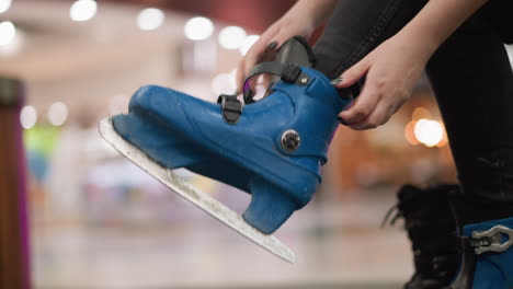 a close-up view of a lady with painted nails removing her blue ice skating shoe, with a blurred background of lights