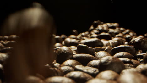 close camera movement through falling fresh coffee beans into a pile of beans laying on a wooden surface