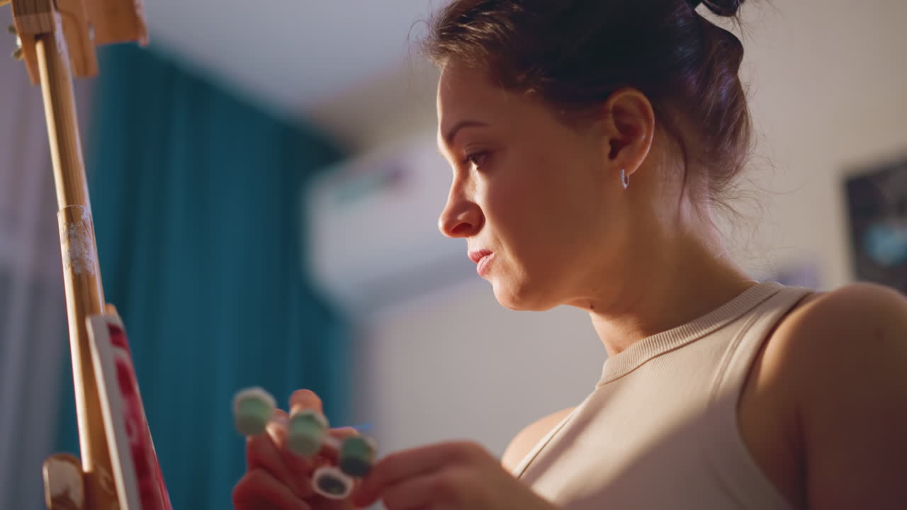 Young Female Painter Concentrating On Detailed Brushwork In Studio, Young Woman Artist Intensely Focusing While Skillfully Blending Pigments With Delicate Strokes In Softly Lit Studio Environment