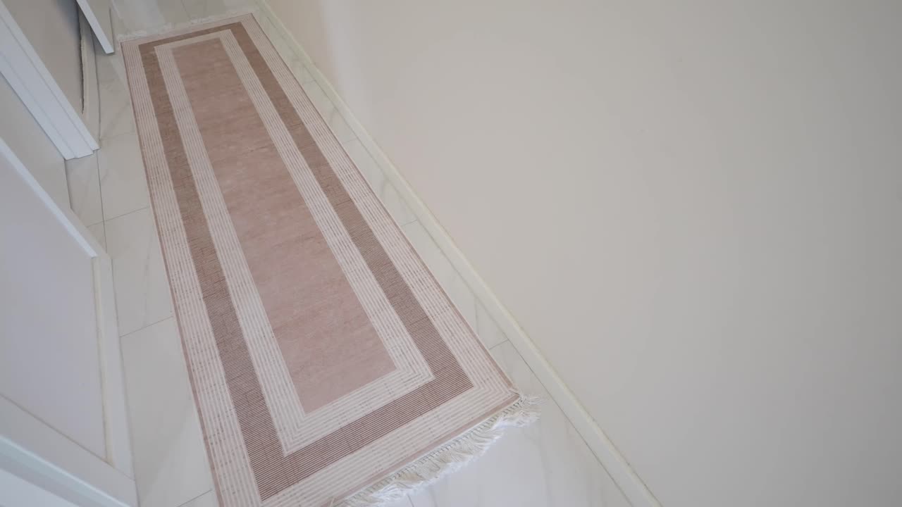 Long beige and pink patterned rug on white tiled floor in a hallway