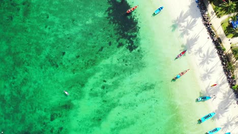 Colorful-fishing-boats-on-shore-of-tropical-island-with-beach-cabins-near-white-sandy-beach-washed-by-turquoise-lagoon-in-Malaysia