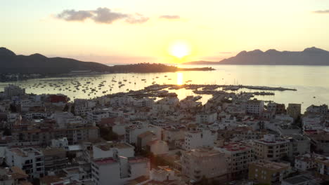 AERIAL:-Port-on-Tropical-Island-with-Boats-and-Ocean-at-Small-Town-at-Sunrise-with-Mountains-in-Background-Vacation,-Travel,-Sunset