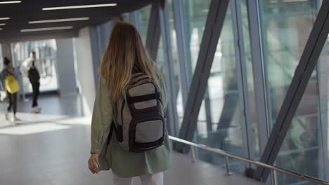 rear view of female tourist carrying backpack walking to gate in airport terminal