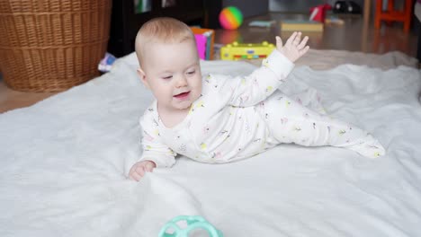 smiling baby girl stretches arms while grabbing mat blanket on ground mattress