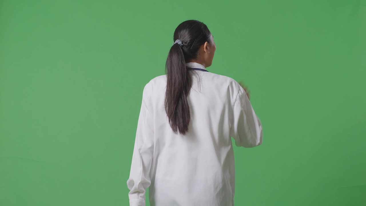 Back View Of Asian Female Doctor With Stethoscope Waving Hand And Smiling While Walking On Green Screen Background In The Hospital