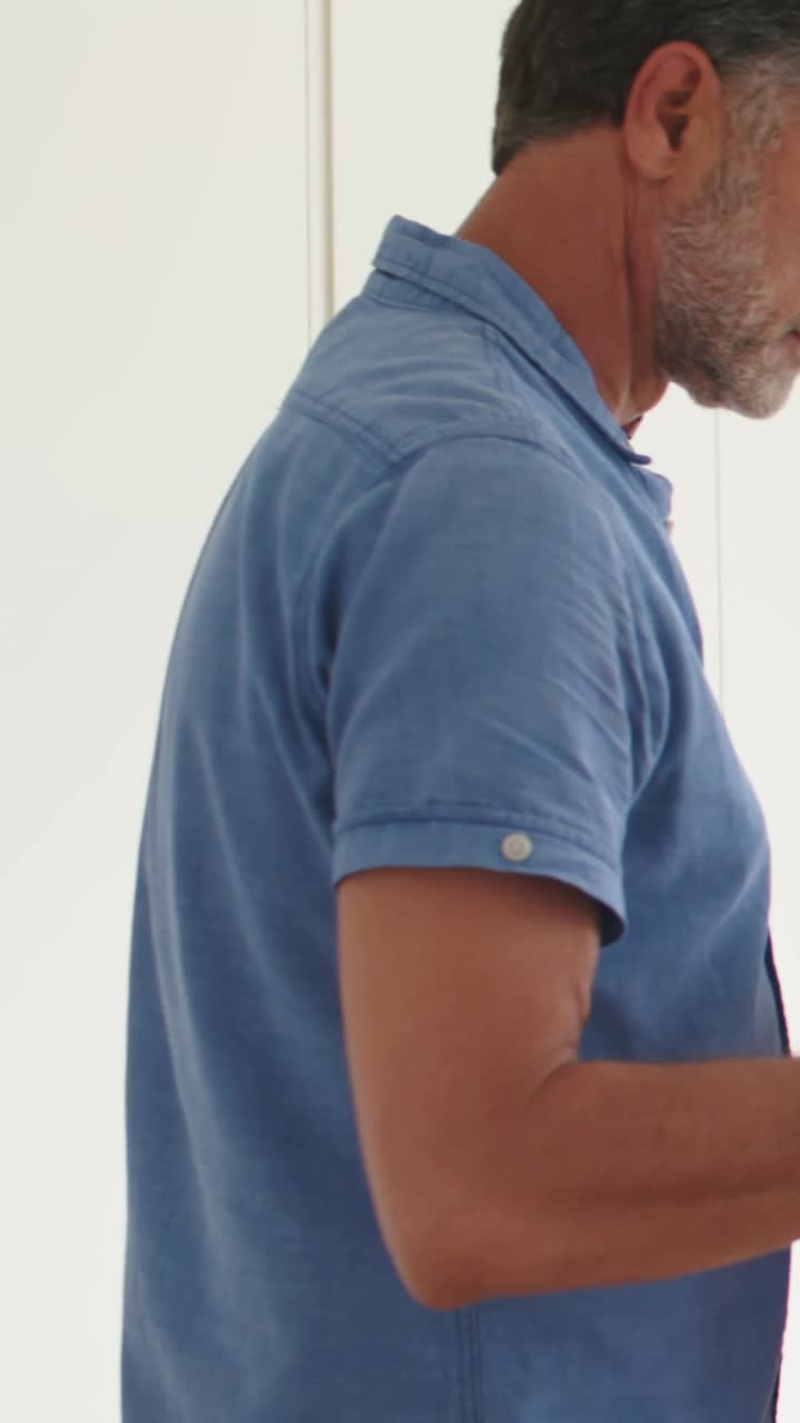 Video verticale: Uomo con polo blu che tiene una felpa rossa, ispeziona mentre rimbocca all'anca a casa, con spazio per il testo.