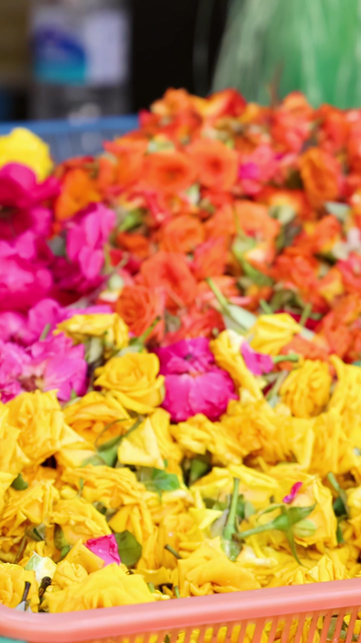 Ghirlande vivaci di fiori di calendula e rose disposte in cesti in un mercato all'aperto a Singapore, riprese con un movimento fluido e laterale della telecamera e luce naturale del giorno.