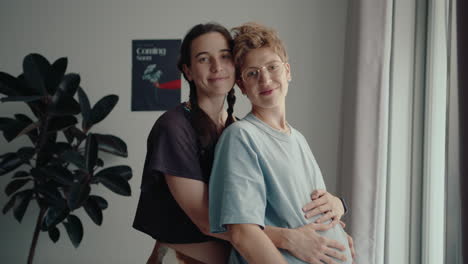 happy lesbian couple expecting baby posing together on camera at home