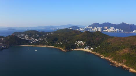 disparo de un dron que viaja hacia adelante sobre una isla tropical con algunos pueblos y una playa entre las montañas y el bosque durante un día soleado-1