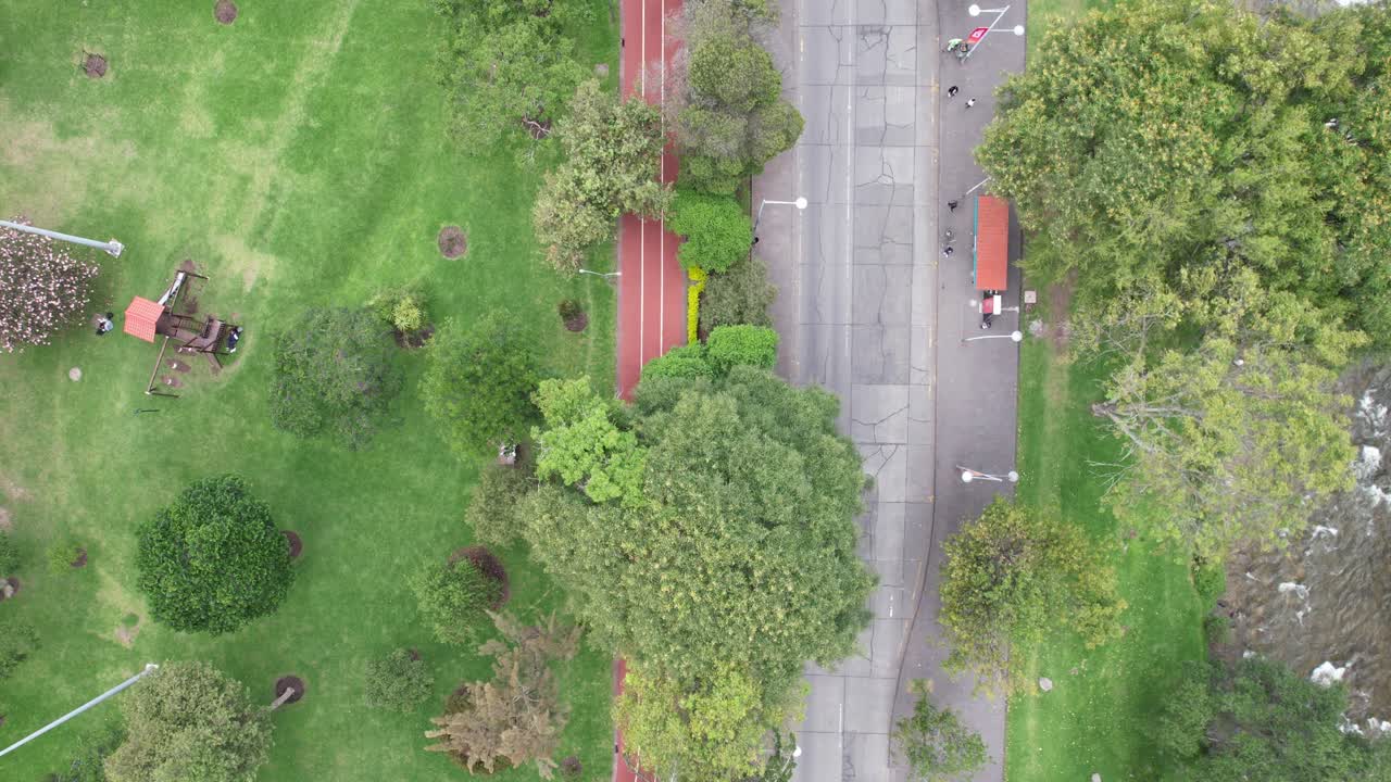 4K aerial drone shot over Parque de la Madre in Cuenca, Ecuador, following the red running track. Shows basketball court, trees, and playground in a vibrant recreational setting.