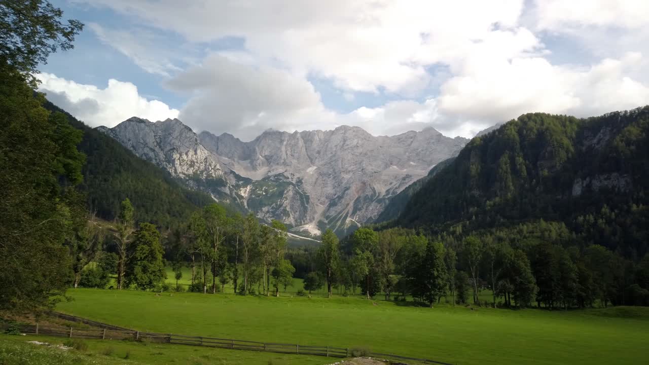 Alpi di Kamnik e della Savinja da Jezersko, Slovenia, nuvole sopra montagne e prati con alberi in primo piano.