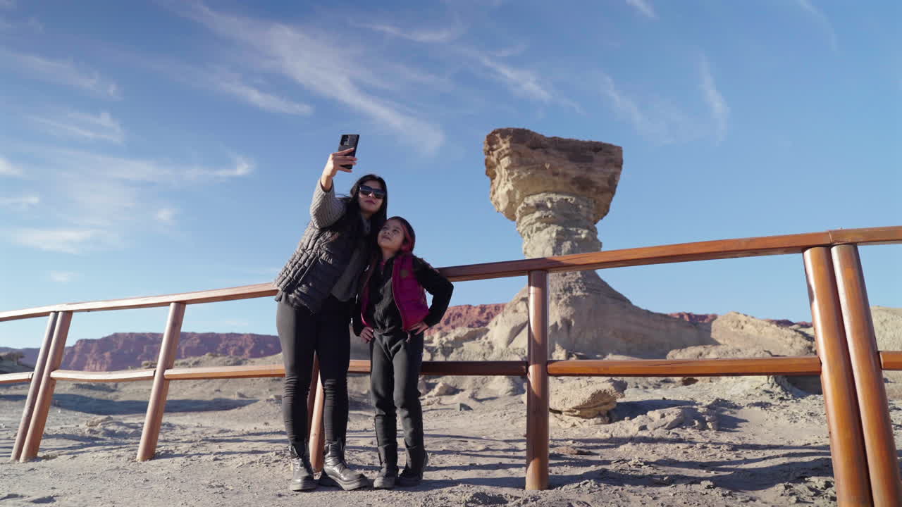 Mother and daughter take a selfie in front of iconic El Hongo rock formation at Ischigualasto Provincial Park, Argentina