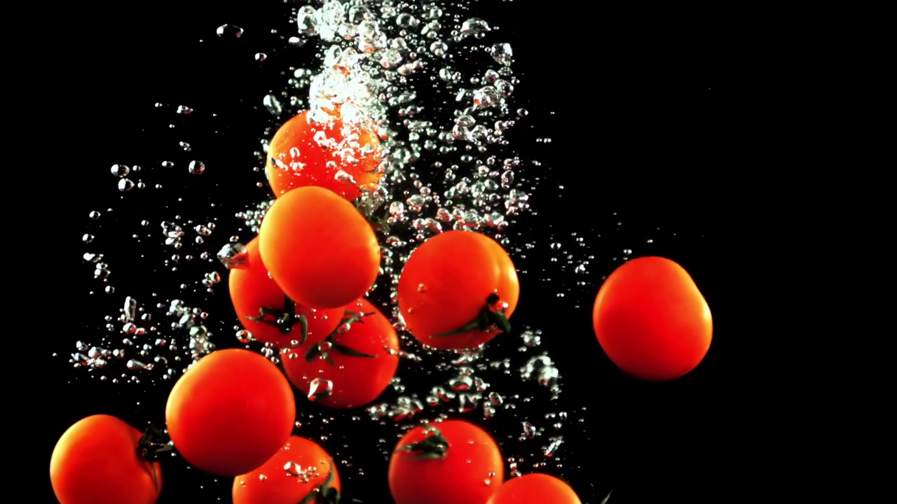 Pomodorini ciliegino rossi freschi che schizzano nell'acqua al rallentatore