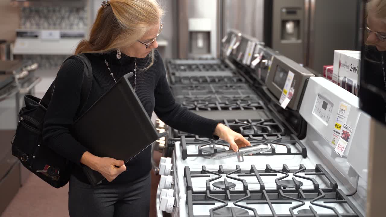 Pretty mature blonde woman looking at the features and benefits of a gas stove in a kitchen appliance store