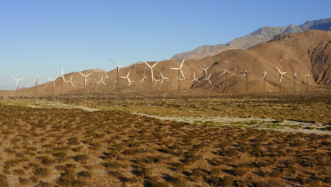 Drone-Volando-Hacia-Docenas-De-Turbinas-Eólicas-En-Un-Enorme-Parque-Eólico-Con-Montañas-En-El-Fondo-Cerca-De-Palm-Springs-En-El-Desierto-De-Mojave,-California,-Ee.uu.