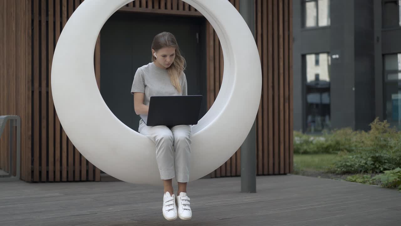 mujer joven con laptop en blanco columpio futurista en el patio al aire libre
