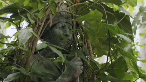 ancient statue covered in vines, hidden in lush forest setting, peaceful and still