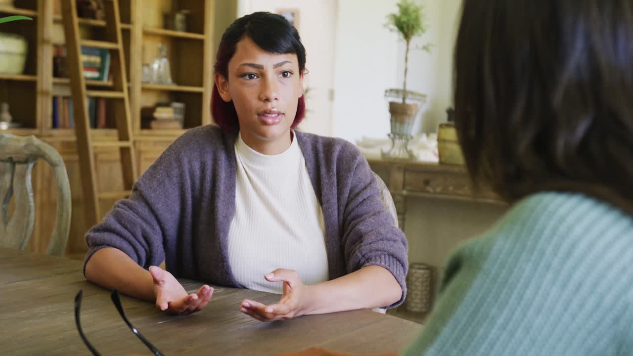Serious biracial sisters sitting at table and talking, in slow motion