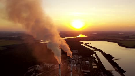pipes with smoke near the evening river. pollution of the environment. industrial plant at sunset. dark smoke coming from plant pipes.