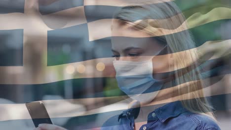 Greece-waving-flag-against-caucasian-woman-wearing-face-mask-using-smartphone-on-the-street